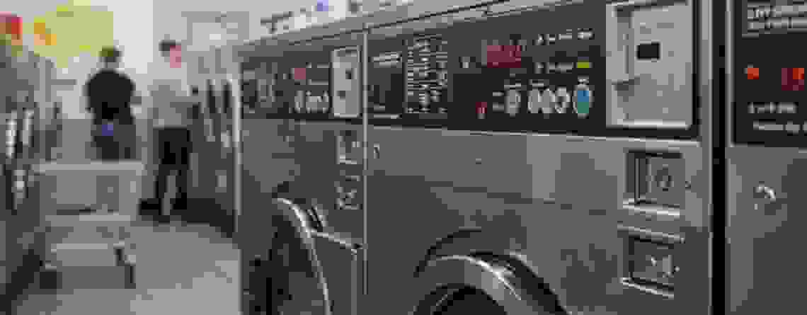 A detailed view of commercial washing machines with coin slots and control panels, illustrating the need for accurate coin handling in high-traffic laundry operations.