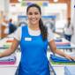 Smiling laundromat employee standing behind neatly folded clothes on tables inside a laundromat.